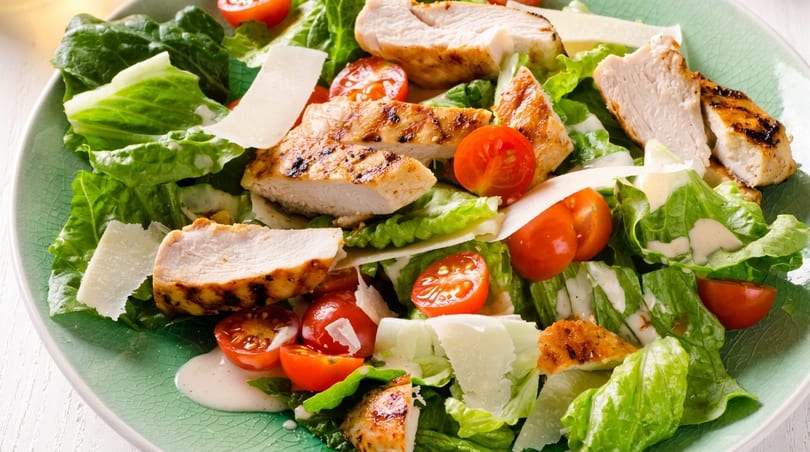 Grilled chicken Caesar salad with romaine lettuce, cherry tomatoes, parmesan, and dressing on a green plate.
