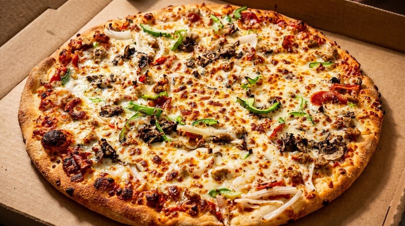 A freshly baked pizza with melted cheese, sausage, mushrooms, onions, and green peppers in a box.