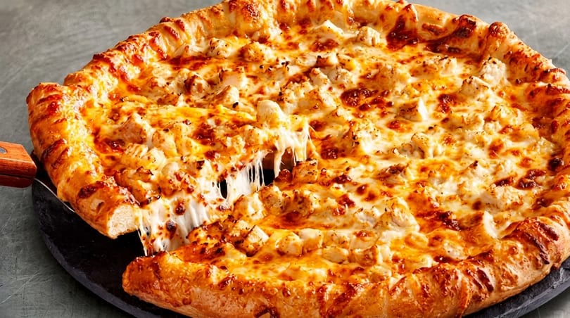 A slice of cheesy chicken pizza being lifted, with melted cheese stretching from the pie.